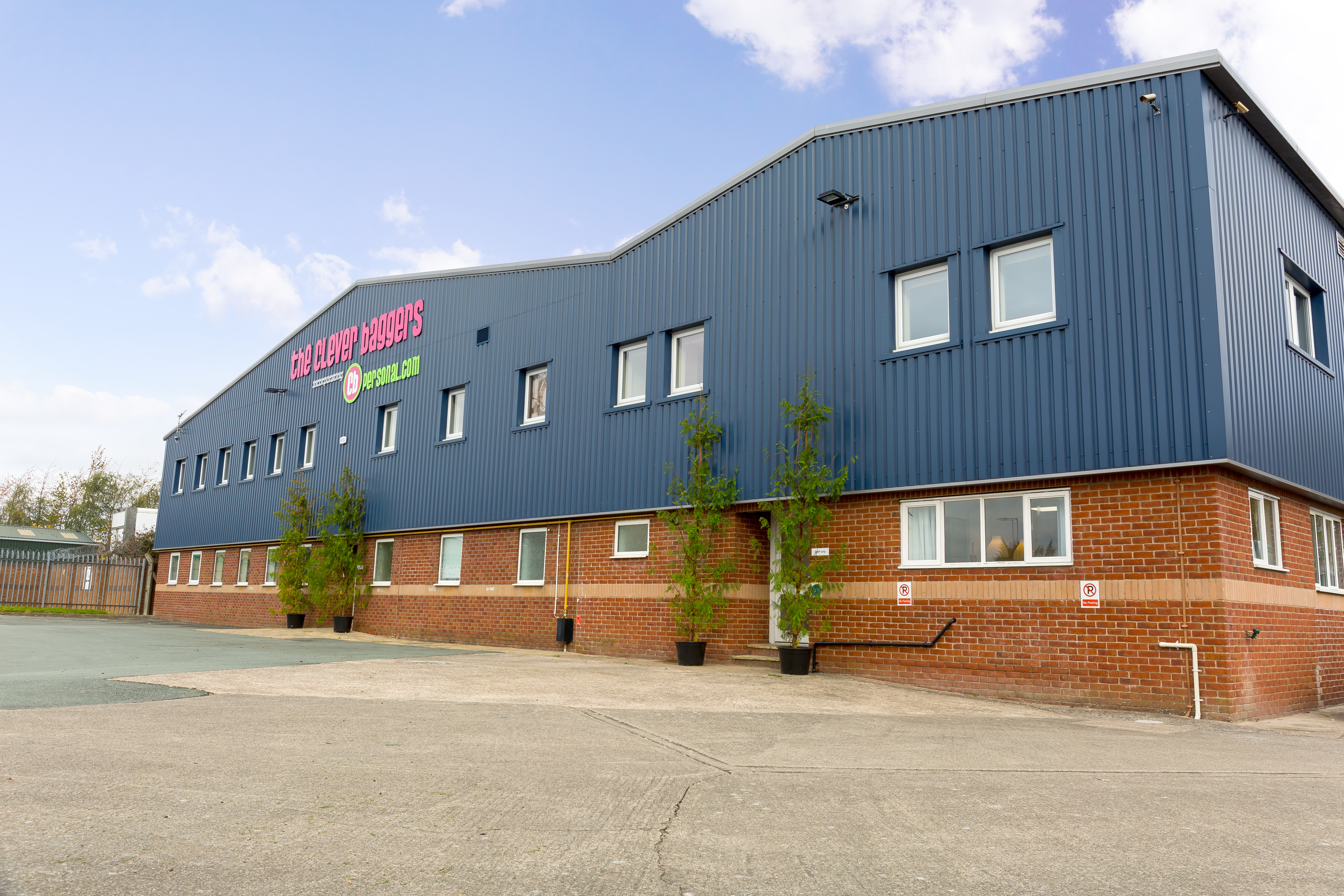 Photo of the outside of The Clever Baggers building. The lower storey is built of brick, the upper storey has dark blue metal cladding with the company name in large bright pink letters across the front.