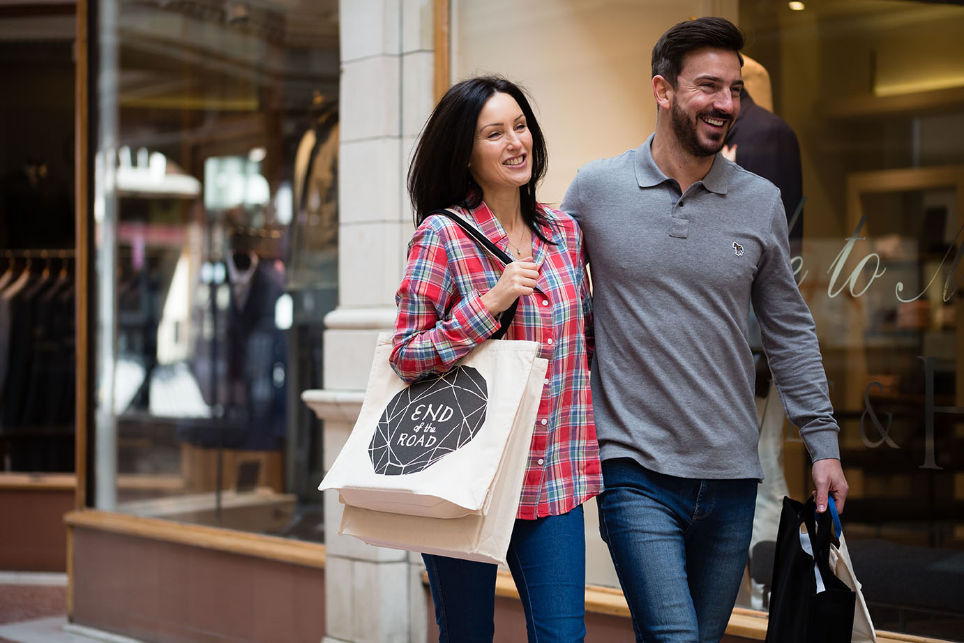 A stylishly dressed couple walking through a shopping precinct carrying their purchases in custom printed canvas tote bags.