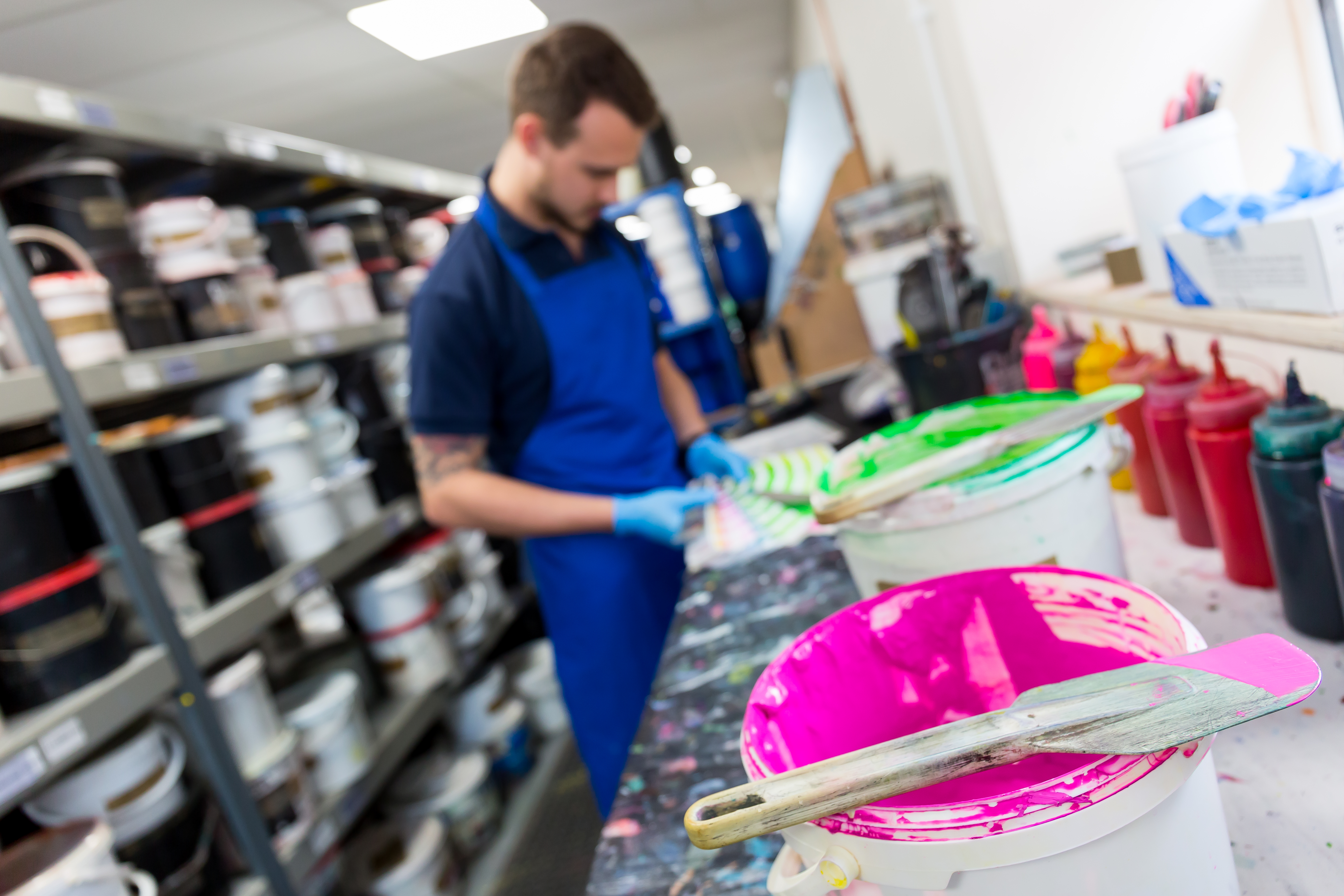 Young white man stood at a bench, checking screen print colours against a Pantone reference book.