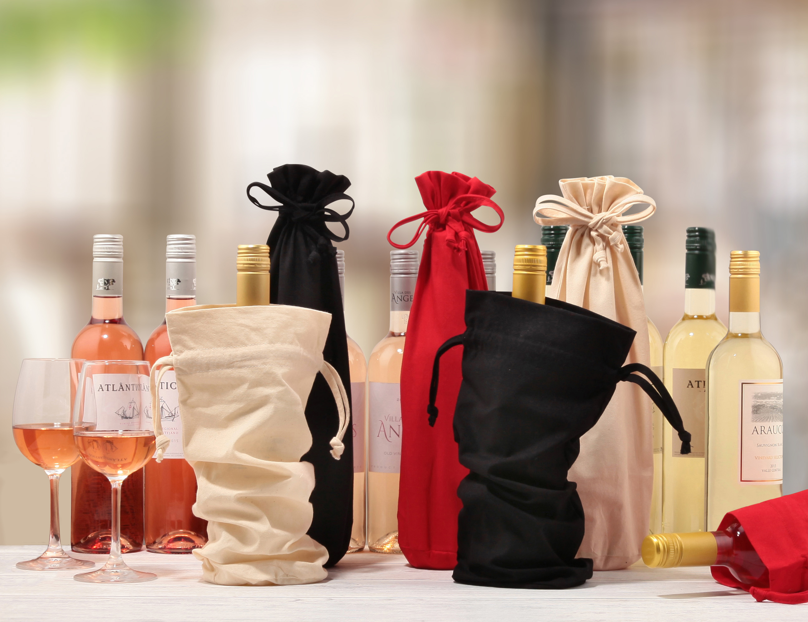 A selection of wine bottles attractively presented with some packaged in cotton bottle gift bags in beige, black, and red cloth colours.