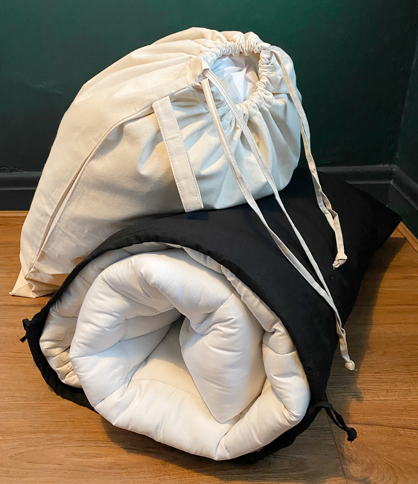 Two cotton drawstring sacks, one in natural beige and the other black, being used to store bedding such as a duvet, pillows, and sheets.
