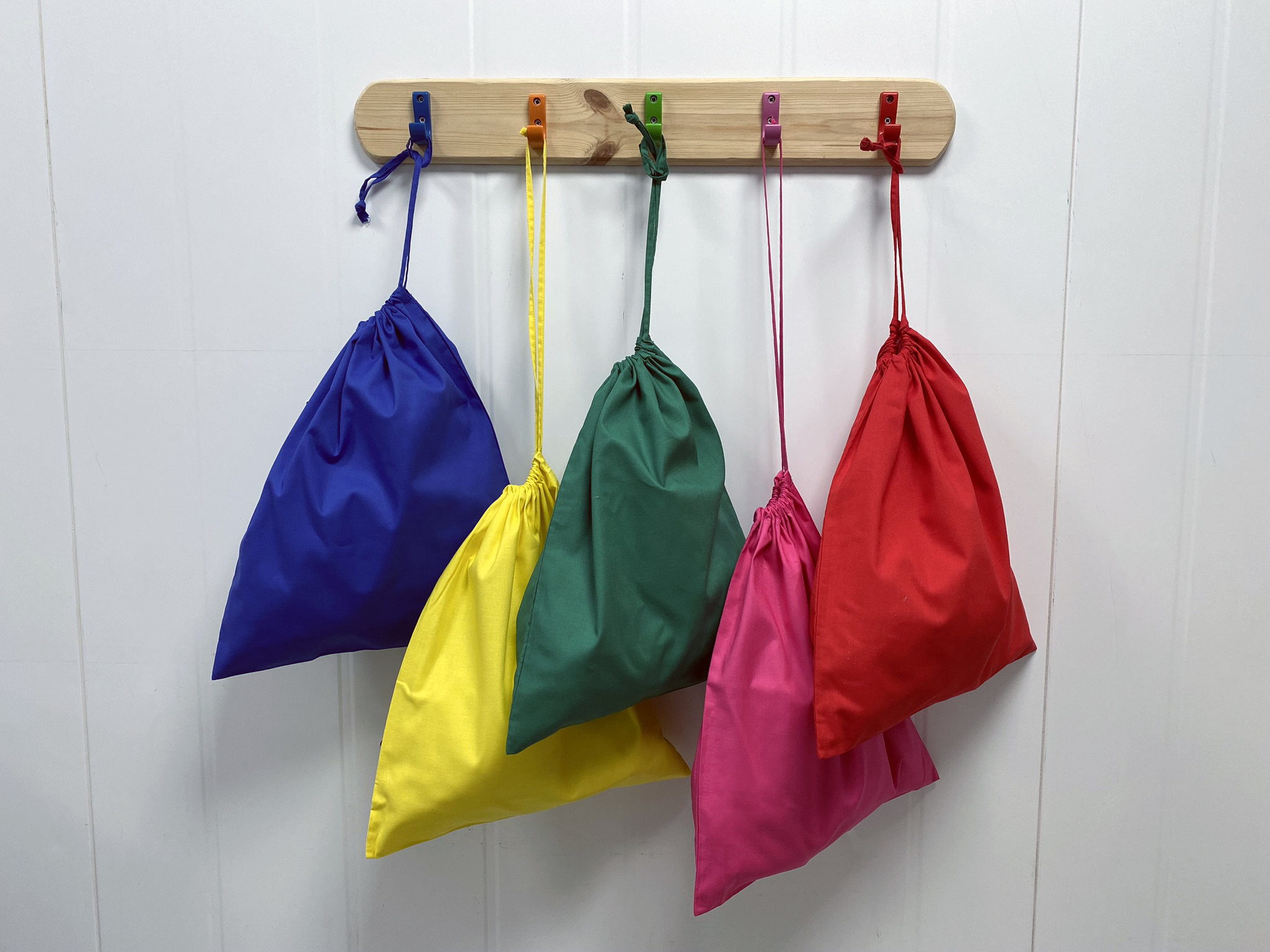 5 colourful drawstring bags hung up on matching pegs