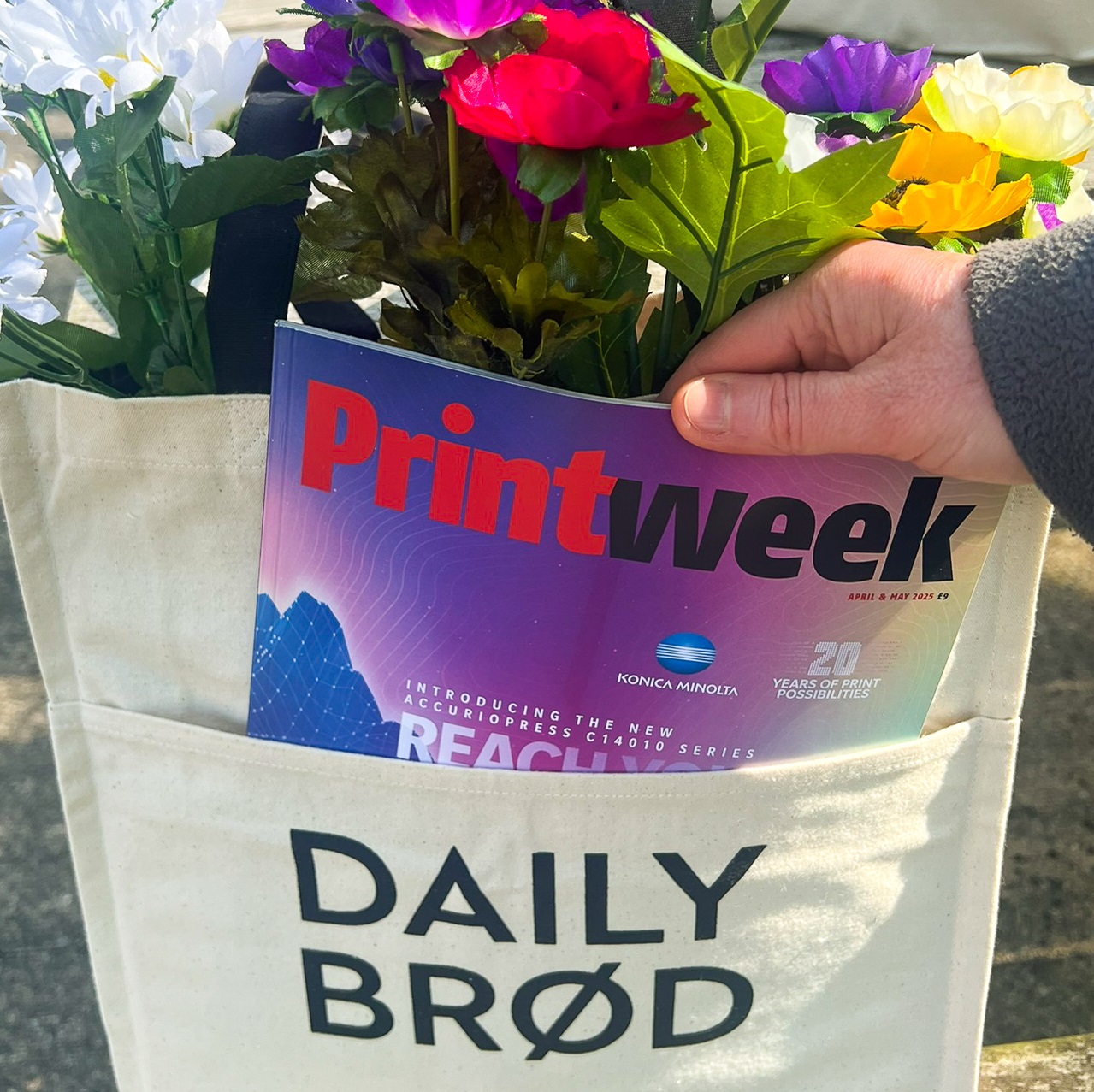 Tote bag holding brightly coloured flowers in the main compartment and magazines in the front pocket.