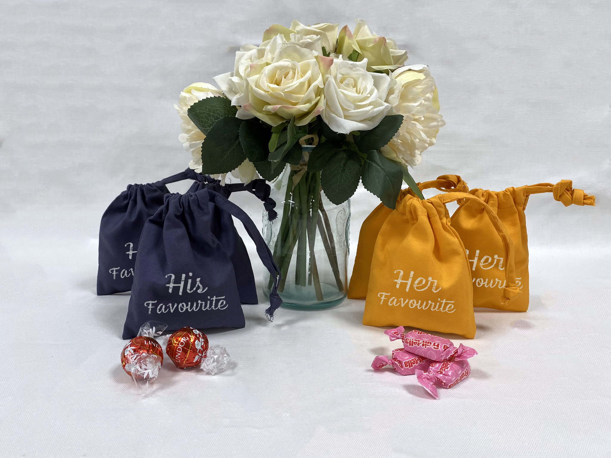 A bouquet of white roses and orange and slate grey bags with sweets placed in front