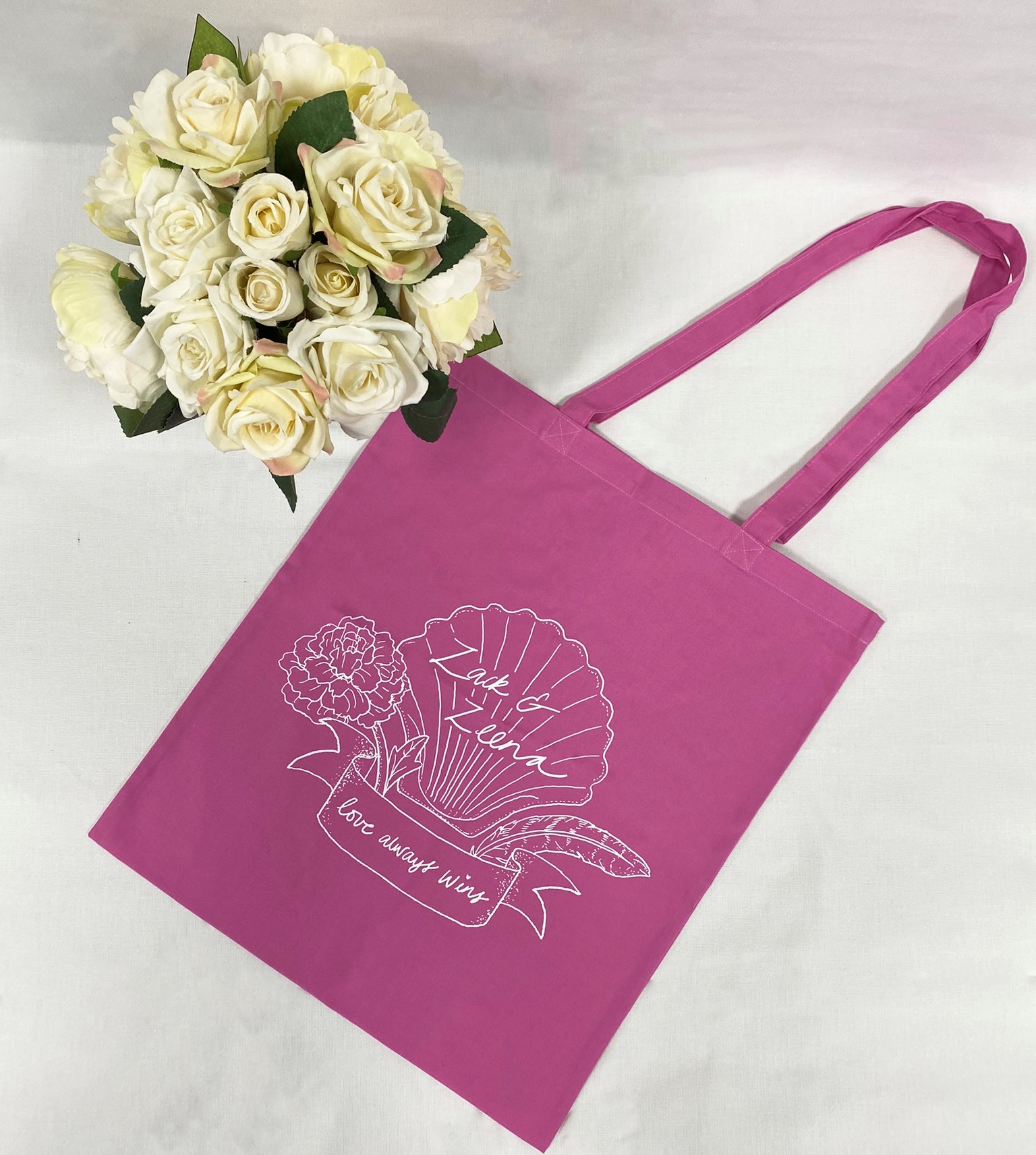 A pink bag with a white design next to a bouquet of flowers