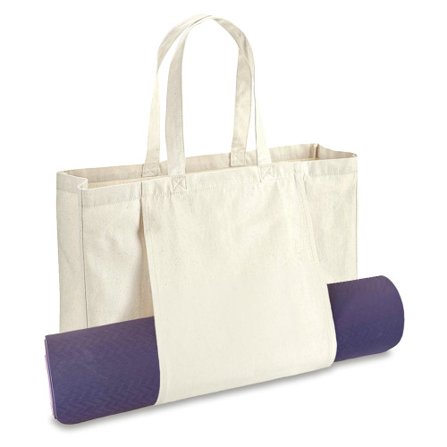 Beige cotton canvas yoga tote bag shown in use with a rolled up yoga mat held by the outer panel.